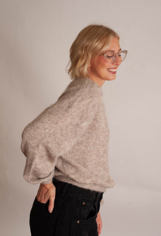 Women modelling a beige cardigan against a neutral photo background. 