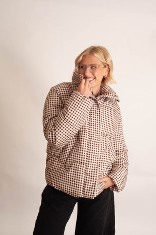 Women modelling a brown checker puffer jacket against a neutral photo backdrop. 