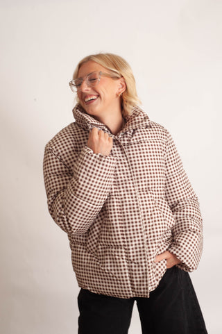 Women modelling a brown checker puffer jacket against a neutral photo backdrop. 