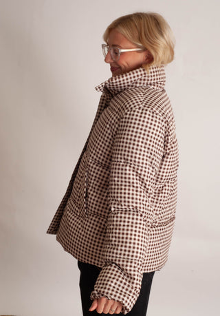 Women modelling a brown checker puffer jacket against a neutral photo backdrop. 