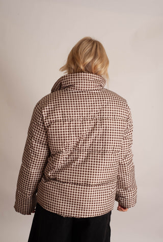 Women modelling a brown checker puffer jacket against a neutral photo backdrop. 