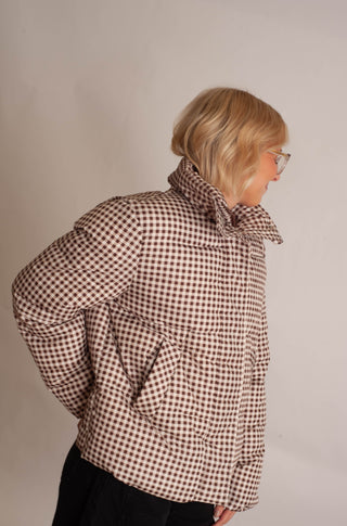 Women modelling a brown checker puffer jacket against a neutral photo backdrop. 