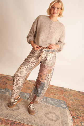 Women modelling paisley printed patchwork pants against a neutral photo backdrop and standing on boho printed rugs. 