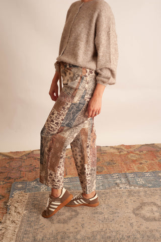 Women modelling paisley printed patchwork pants against a neutral photo backdrop and standing on boho printed rugs. 