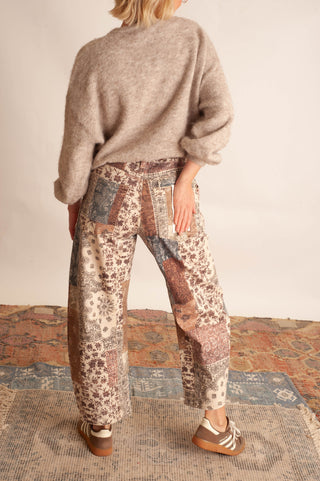 Women modelling paisley printed patchwork pants against a neutral photo backdrop and standing on boho printed rugs. 