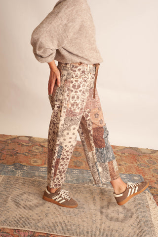 Women modelling paisley printed patchwork pants against a neutral photo backdrop and standing on boho printed rugs. 