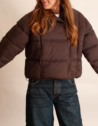 Women modelling a brown puffer jacket against a neutral photo background. 