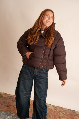 Women modelling a brown puffer jacket against a neutral photo background. 
