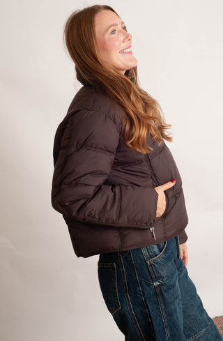 Women modelling a brown puffer jacket against a neutral photo background. 