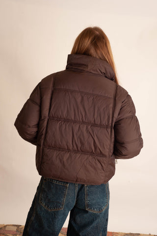 Women modelling a brown puffer jacket against a neutral photo background. 
