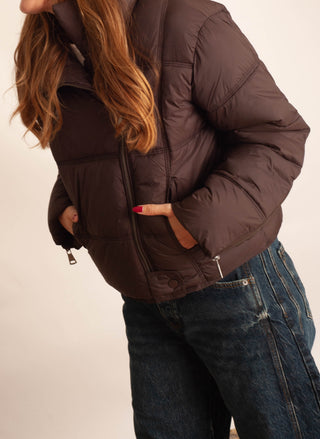 Women modelling a brown puffer jacket against a neutral photo background. 