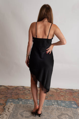 Women wearing a black lace trim sating dress against a neutral photo backdrop standing on boho inspired rugs. 