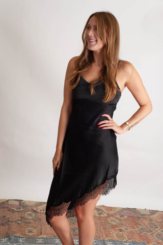 Women wearing a black lace trim sating dress against a neutral photo backdrop standing on boho inspired rugs. 