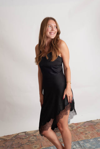 Women wearing a black lace trim sating dress against a neutral photo backdrop standing on boho inspired rugs. 