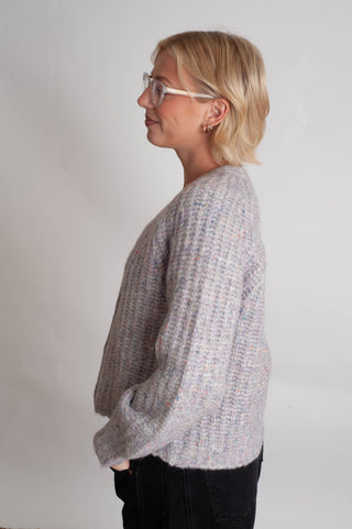 Women modelling a purple confetti cardigan against a neutral photo back drop. 