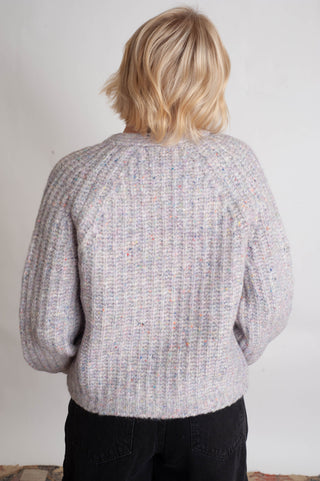 Women modelling a purple confetti cardigan against a neutral photo back drop. 