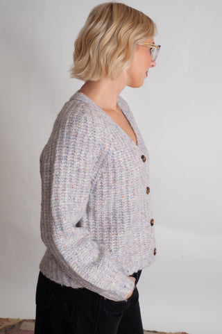 Women modelling a purple confetti cardigan against a neutral photo back drop. 