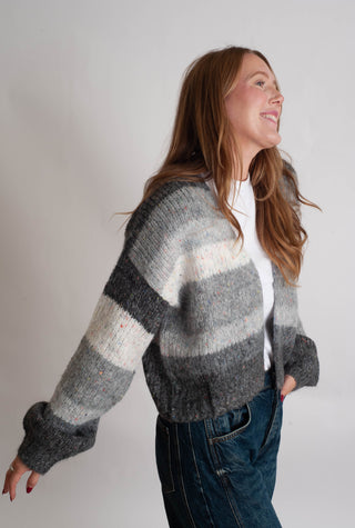 Women modelling a grey striped cardigan against a neutral photo backdrop. 