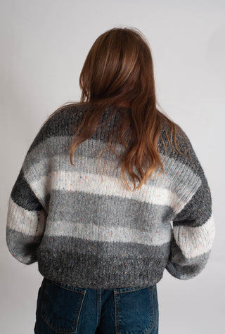 Women modelling a grey striped cardigan against a neutral photo backdrop. 
