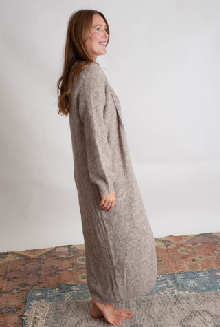 Women modelling a long beige cardigan against a neutral photo backdrop standing on boho inspired printed rugs. 