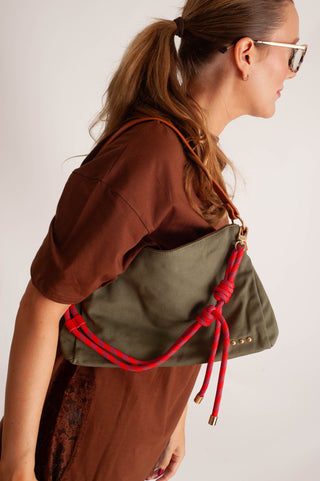 A woman in a brown t-shirt wearing an olive green canvas shoulder bag with a prominent red rope handle and gold-tone hardware, shown from a side profile against a light gray background.