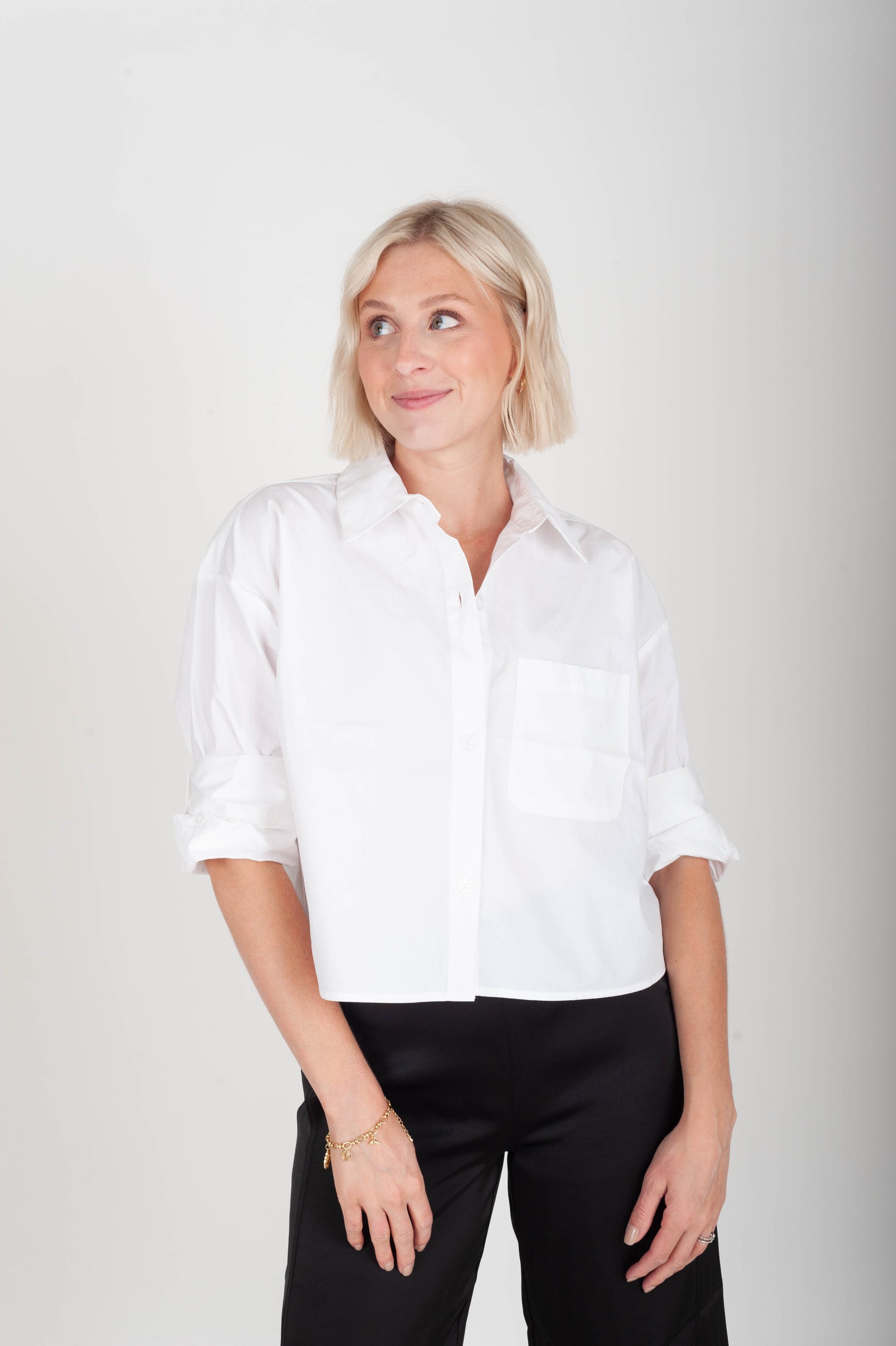 Woman wearing a white shirt and black pants against a plain background