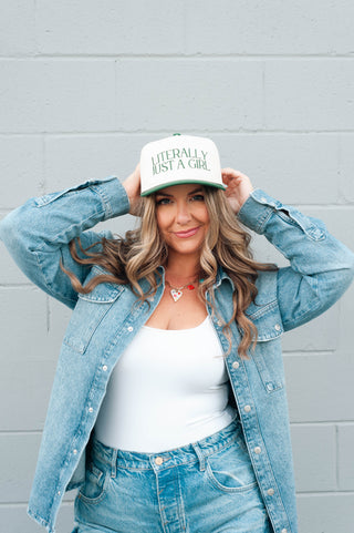 Woman wearing a denim jacket and jeans with a white cap in front of a gray wall