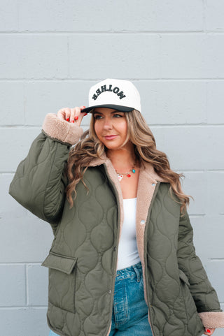 Woman wearing a green quilted jacket and white cap with 'Barlow' branding against a gray wall.