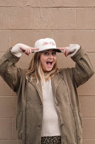 Person wearing a cap with text, standing against a beige brick wall