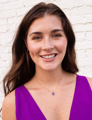 Woman wearing a purple top and necklace with a white brick wall background