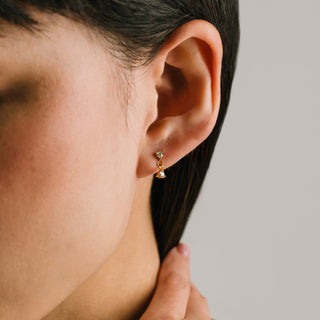 Close-up of an ear wearing a gold earring with a small gemstone on a neutral background