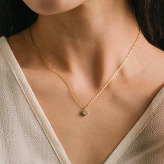 Close-up of a gold necklace with a small pendant on a person wearing a beige top.