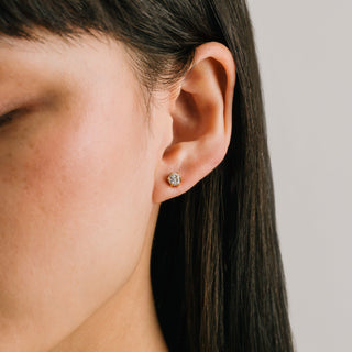 Close-up of an ear wearing a diamond stud earring with a neutral background