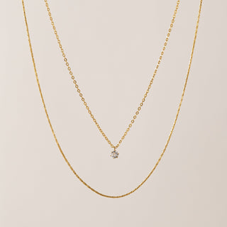 Gold necklace with a small diamond pendant on a beige background
