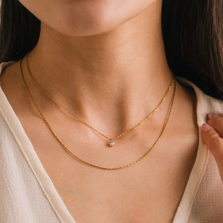 Close-up of a person wearing a gold necklace with a small pendant.