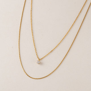 Gold chain necklace with a small round pendant on a beige background