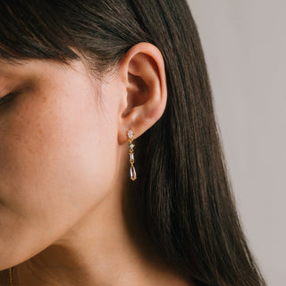 Close-up of an ear wearing a gold earring with gemstones on a neutral background