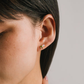 Close-up of a person wearing a gold earring with a green gemstone on a neutral background