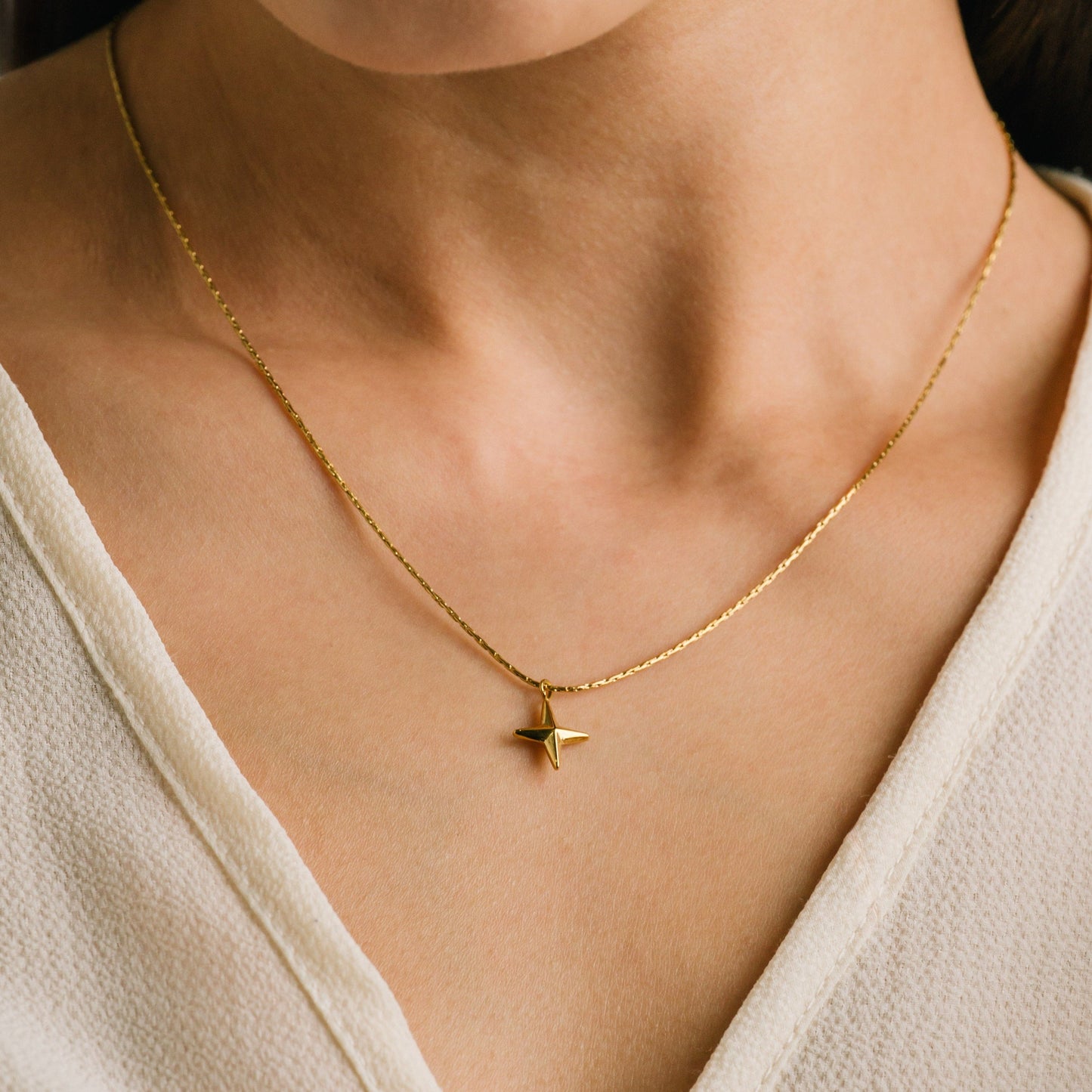 Gold necklace with a star pendant on a person wearing a white top.
