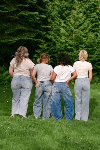 Four women wearing blue jeans in the grass facing away from the camera. 