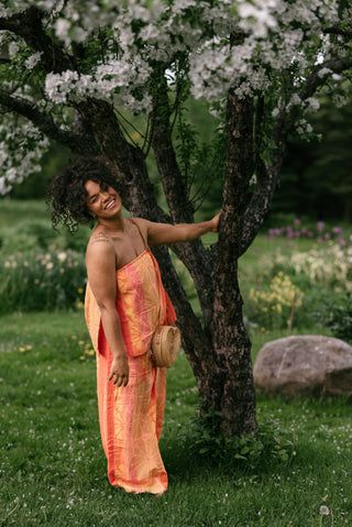 Women wearing an orange matching top and pant set with a wicker bag under a cherry blossom tree.