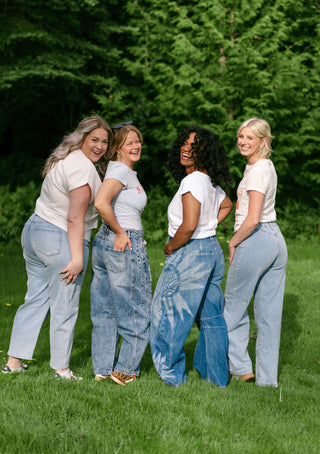 Four women wearing jeans and white tees in a garden.