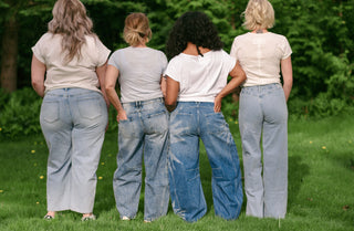 Four women wearing blue jeans in the grass facing away from the camera. 