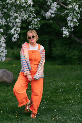 Women wearing orange overalls and a rainbow cardigan in a garden. 