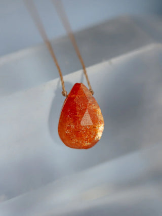 Orange teardrop-shaped pendant on a chain against a light background