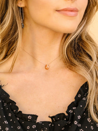 Close-up of a woman wearing a black top with floral patterns and a necklace with a teardrop-shaped pendant.