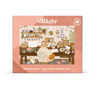 A 1000-piece jigsaw puzzle box by Villager, featuring a warm, cozy illustration of a woman sewing in a decorated craft room with a cat. The box has a dusty pink border and is shown against a plain white background.