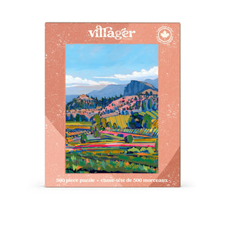 A boxed jigsaw puzzle set by villager, featuring a colorful landscape illustration of vineyard fields and mountains, styled on a light pink background with scattered puzzle pieces and small decorative props.