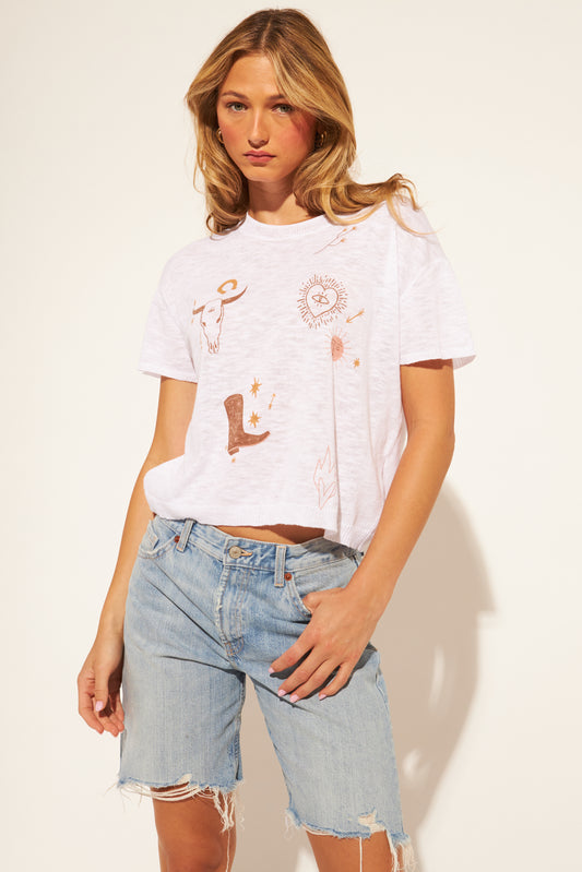 Woman wearing a white t-shirt with graphics and light blue denim shorts on a plain background