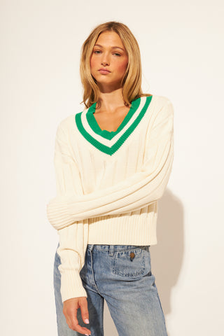 Woman wearing a cream sweater with green trim against a white background
